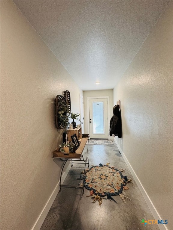 doorway to outside featuring concrete flooring, baseboards, a textured wall, and a textured ceiling