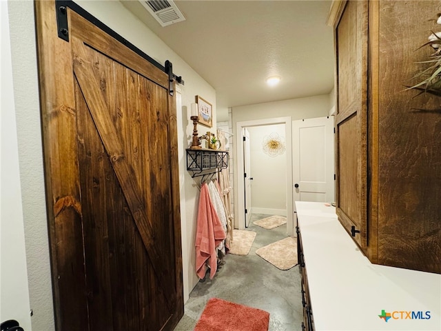 corridor featuring visible vents, a barn door, and unfinished concrete floors