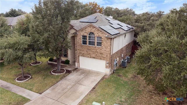 view of front facade with central AC, solar panels, a garage, and a front lawn