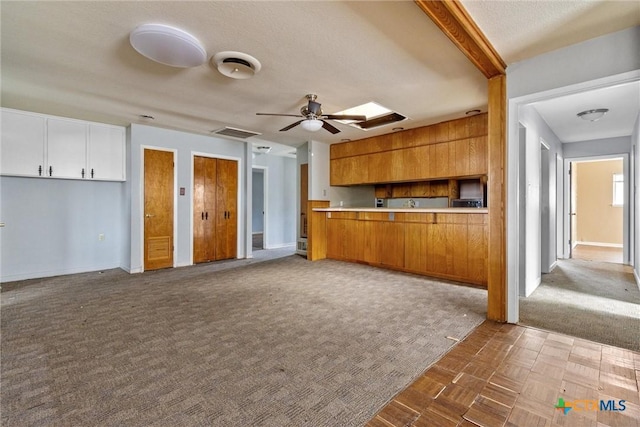 kitchen with ceiling fan, kitchen peninsula, a skylight, a textured ceiling, and white cabinets