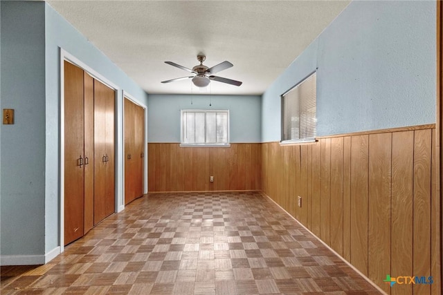 spare room with ceiling fan, wood walls, and light parquet floors