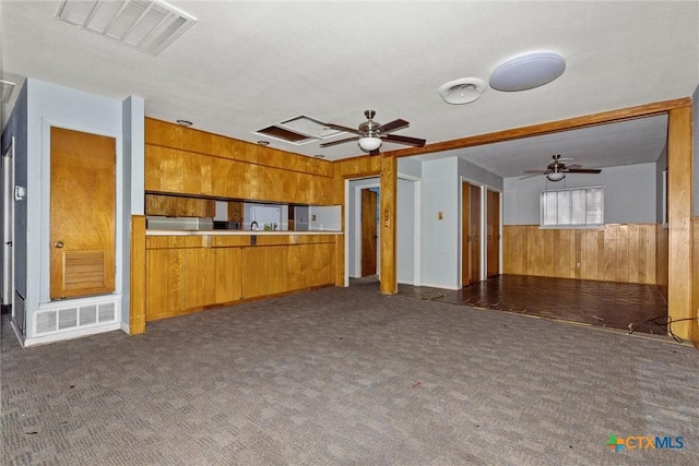 unfurnished living room with ceiling fan, dark carpet, and wood walls