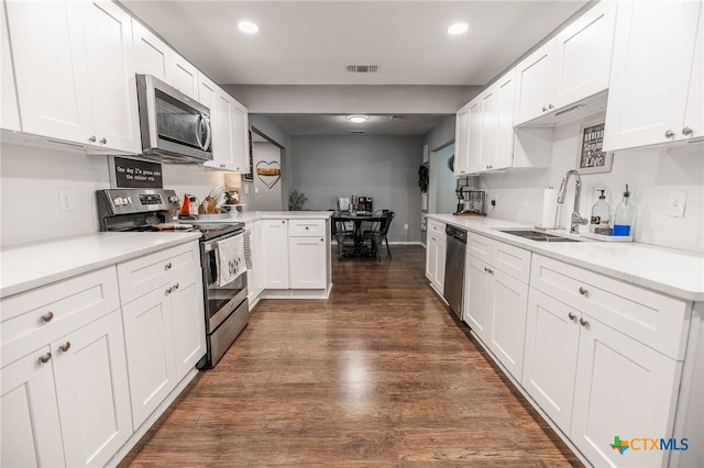 kitchen with kitchen peninsula, stainless steel appliances, dark wood-type flooring, sink, and white cabinets