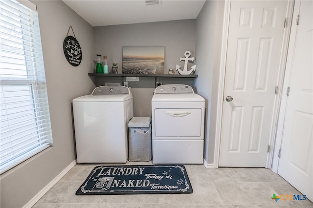 laundry room with light tile patterned flooring, washing machine and dryer, and a wealth of natural light