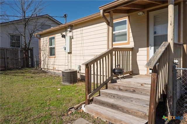 entrance to property featuring cooling unit, a lawn, and fence