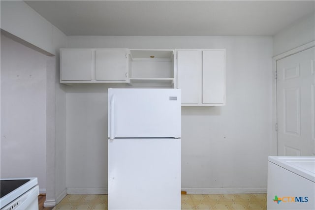 kitchen with white appliances, light floors, baseboards, washer / dryer, and white cabinets