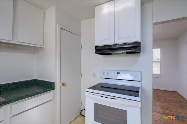 kitchen featuring light wood-style flooring, under cabinet range hood, dark countertops, white cabinetry, and white electric stove