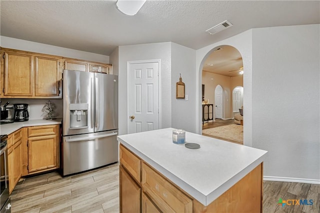 kitchen with stainless steel refrigerator with ice dispenser, visible vents, arched walkways, light countertops, and light wood-style flooring