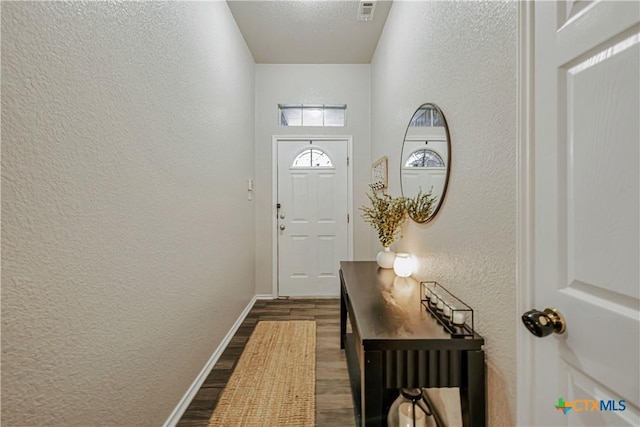 doorway to outside with baseboards, a textured wall, visible vents, and dark wood-type flooring