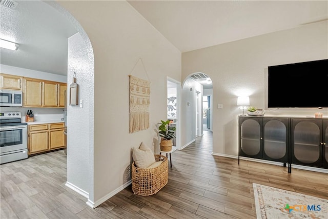 corridor with light wood-type flooring, arched walkways, and baseboards