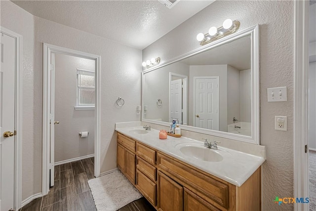 full bath featuring double vanity, a sink, and a textured wall