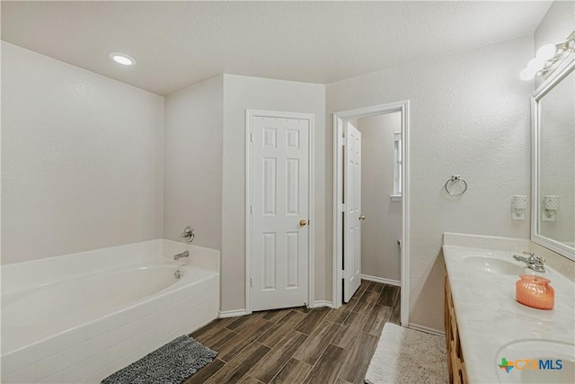 bathroom featuring double vanity, a sink, wood finished floors, and a garden tub