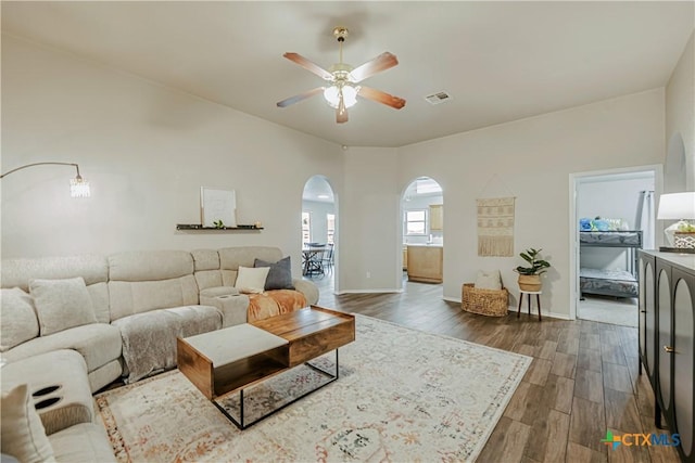 living area featuring baseboards, arched walkways, a ceiling fan, and dark wood-style floors