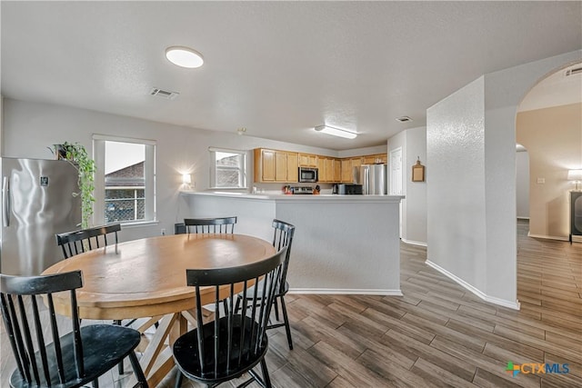 dining room with arched walkways, baseboards, light wood-style flooring, and visible vents
