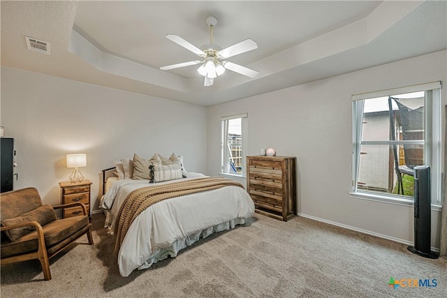 carpeted bedroom with baseboards, a ceiling fan, a tray ceiling, and visible vents