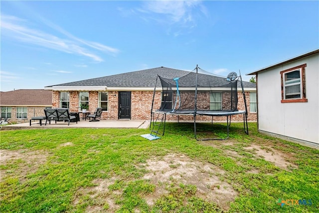 rear view of property featuring a lawn, a trampoline, brick siding, and a patio