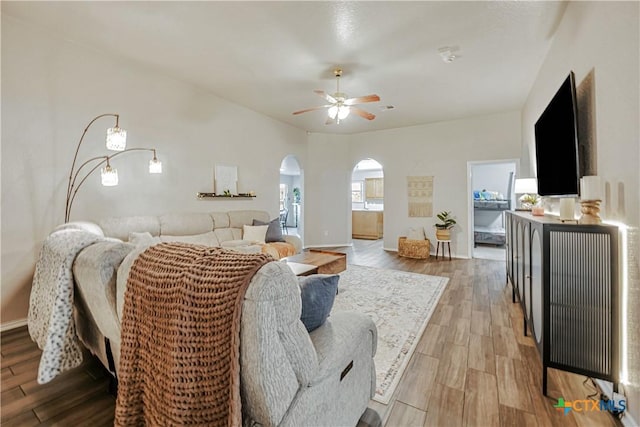 living area featuring arched walkways, ceiling fan, baseboards, and light wood finished floors