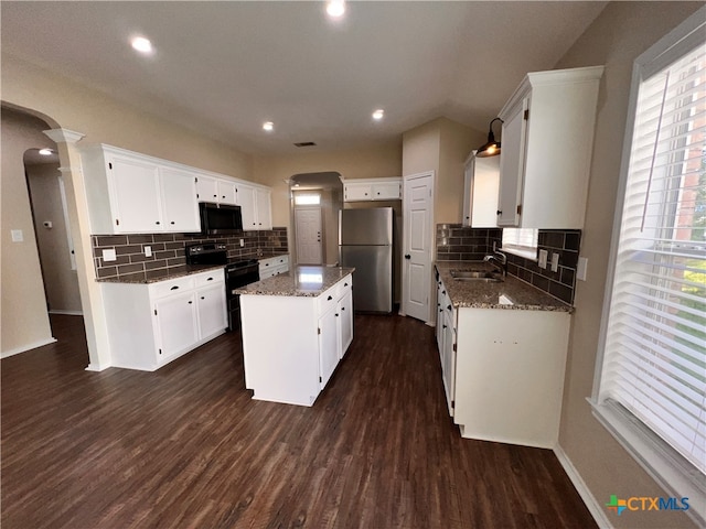 kitchen with a wealth of natural light, black / electric stove, stainless steel fridge, and a center island