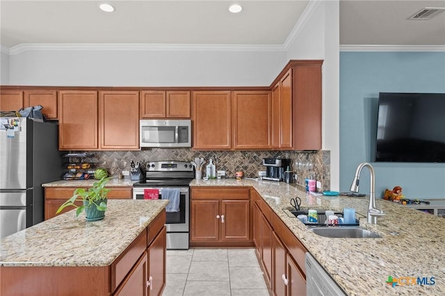 kitchen with appliances with stainless steel finishes, a sink, light stone counters, brown cabinetry, and crown molding