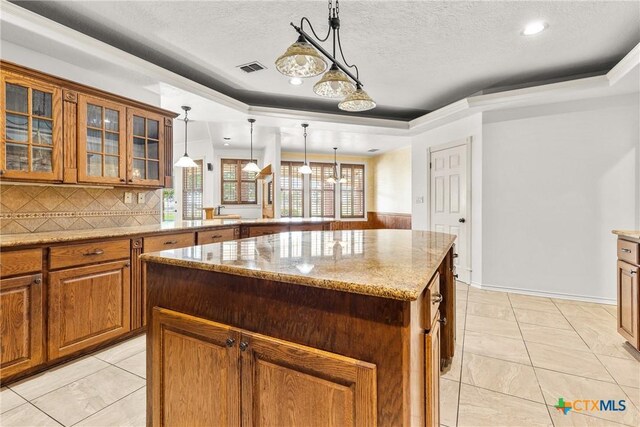 803 S Converse St, Flatonia, TX 78941 - kitchen with a chandelier, brown cabinetry, light stone countertops, a kitchen island, and glass insert cabinets