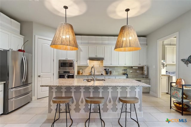 kitchen with stainless steel appliances, light stone countertops, a kitchen island with sink, and white cabinets