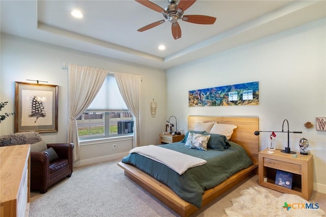 bedroom with a raised ceiling, light colored carpet, and ceiling fan