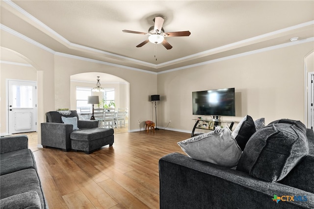 living room featuring wood-type flooring, ceiling fan with notable chandelier, a tray ceiling, and crown molding