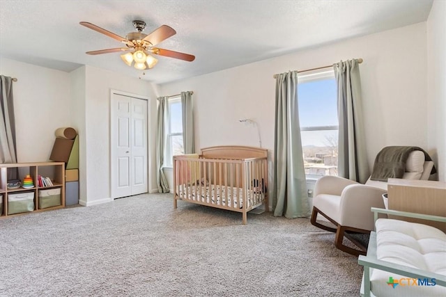 carpeted bedroom featuring a crib, ceiling fan, and a closet