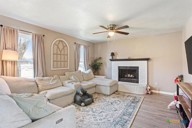 living room with ceiling fan, a fireplace, a textured ceiling, and light wood-type flooring