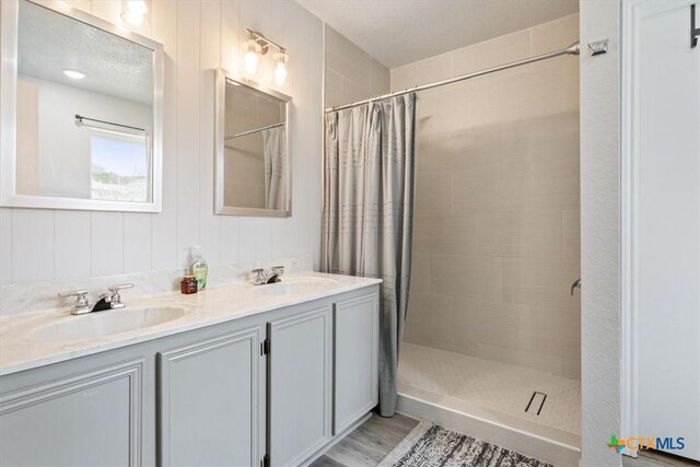 full bathroom featuring double vanity, a tile shower, and a sink
