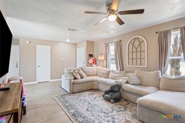 living room featuring ceiling fan, a textured ceiling, and light wood-type flooring