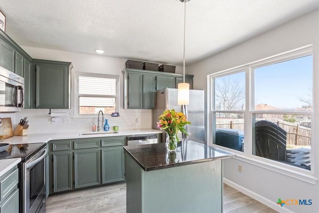 kitchen with sink, a center island, light wood-type flooring, appliances with stainless steel finishes, and pendant lighting