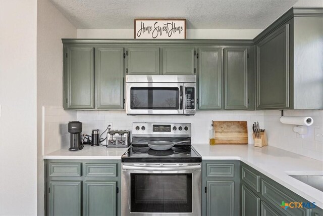kitchen with light countertops, a textured ceiling, green cabinetry, backsplash, and stainless steel appliances