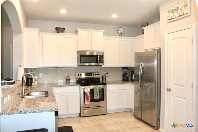 kitchen featuring a sink, light stone counters, backsplash, white cabinetry, and appliances with stainless steel finishes