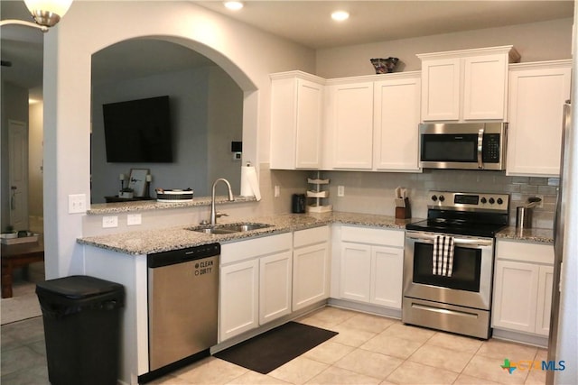 kitchen with backsplash, light stone counters, stainless steel appliances, white cabinetry, and a sink