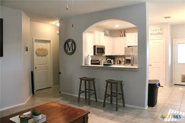 kitchen with visible vents, arched walkways, stainless steel appliances, white cabinetry, and a kitchen breakfast bar