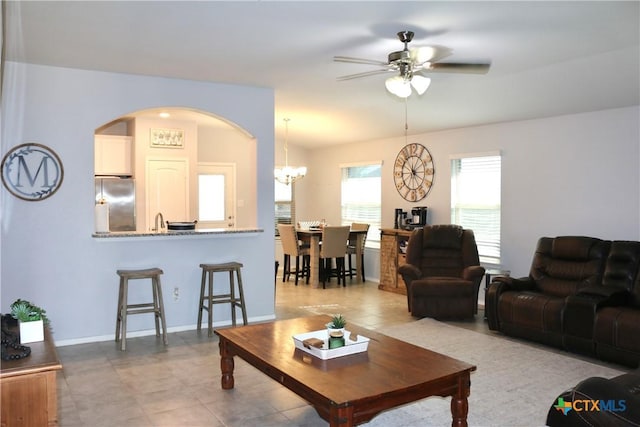 living area featuring ceiling fan with notable chandelier and baseboards