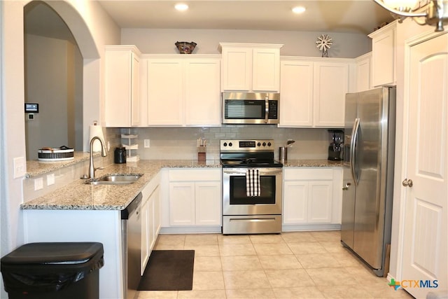 kitchen featuring light stone countertops, a sink, appliances with stainless steel finishes, white cabinetry, and tasteful backsplash