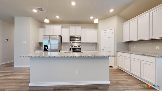 kitchen featuring white cabinets, decorative light fixtures, a center island with sink, and appliances with stainless steel finishes