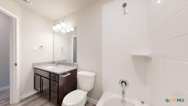 full bathroom featuring hardwood / wood-style floors, tiled shower / bath combo, toilet, and vanity