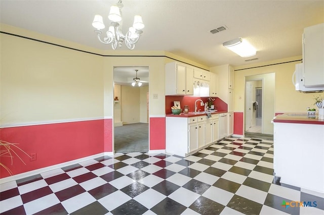 kitchen featuring ceiling fan with notable chandelier, a sink, white cabinetry, visible vents, and tile patterned floors