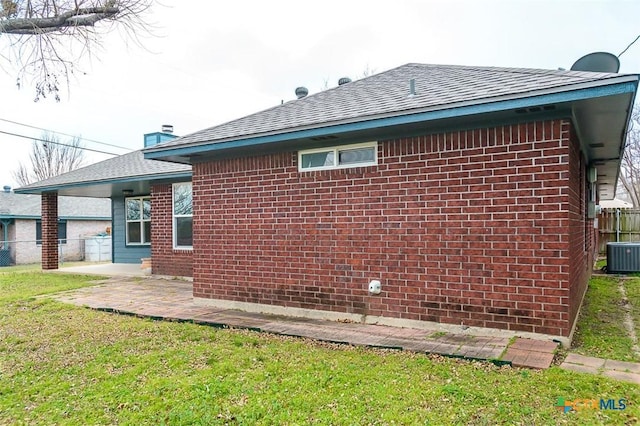 view of side of home with a yard, brick siding, roof with shingles, and fence