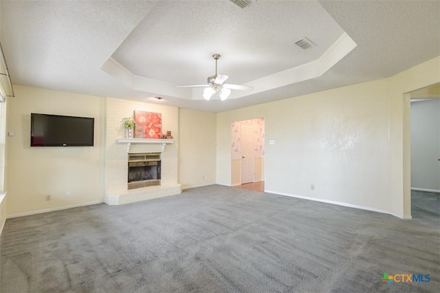 unfurnished living room with a textured ceiling, a tray ceiling, a fireplace, and visible vents