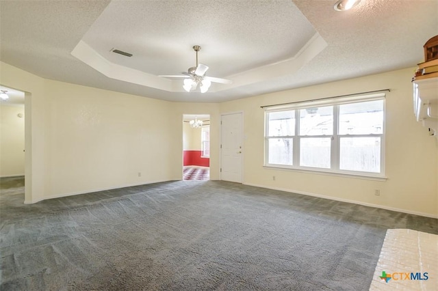 empty room with visible vents, dark carpet, a raised ceiling, and a textured ceiling