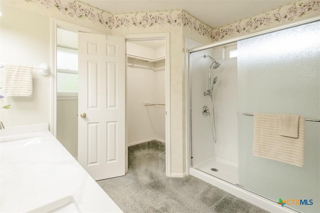 bathroom featuring a spacious closet, a stall shower, and a sink