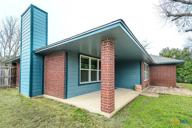 view of property exterior with a patio area, a chimney, fence, and a lawn