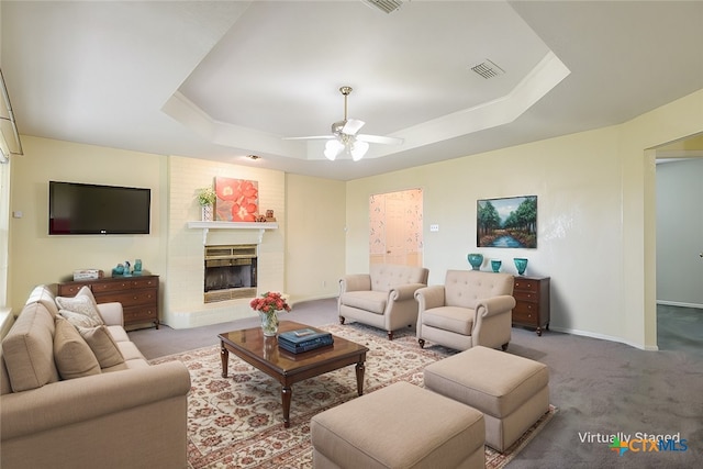 carpeted living room featuring baseboards, visible vents, a raised ceiling, a ceiling fan, and a fireplace