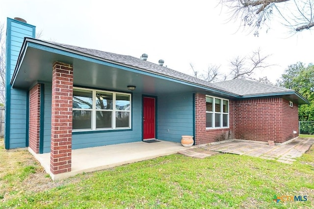 view of front of home featuring roof with shingles, a front yard, a patio, and brick siding