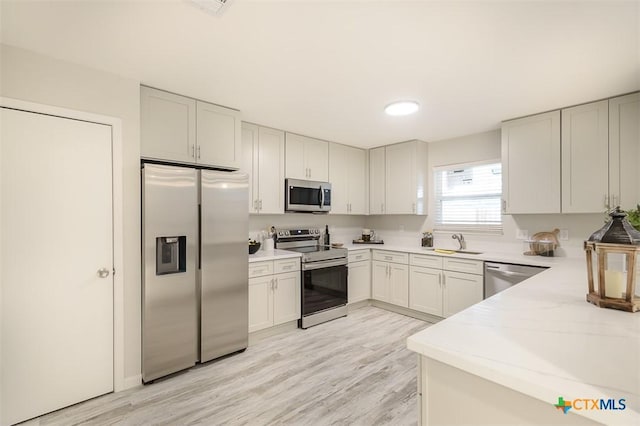 kitchen with appliances with stainless steel finishes, white cabinetry, sink, light stone counters, and light wood-type flooring