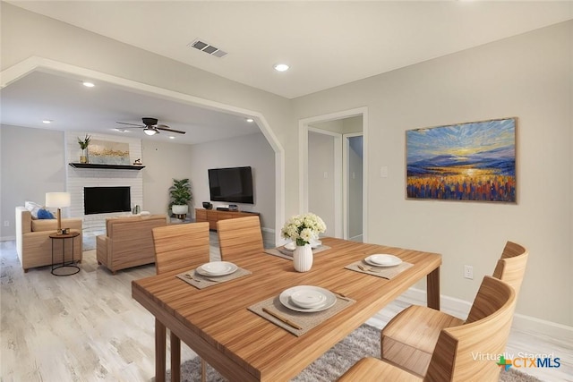 dining space featuring a fireplace, ceiling fan, and light wood-type flooring